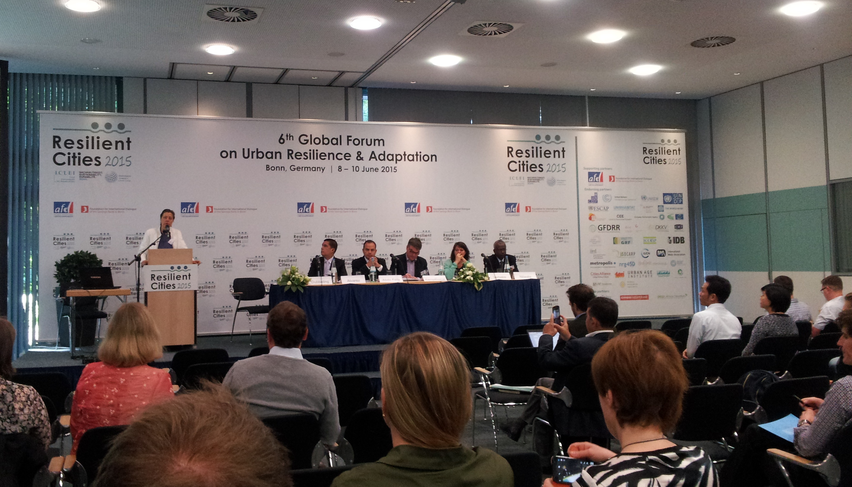 Auf dem Foto ist ein Podium des Urban Food Forums auf dem Kongress Resilient Cities 2015 zu sehen. Darauf sitzen mehrere Menschen; eine Frau spricht zum Publikum im Vordergrund.